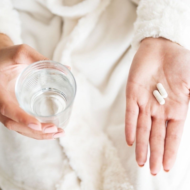 Complément alimentaire pour la peau dans une main de femme avec un verre d'eau
